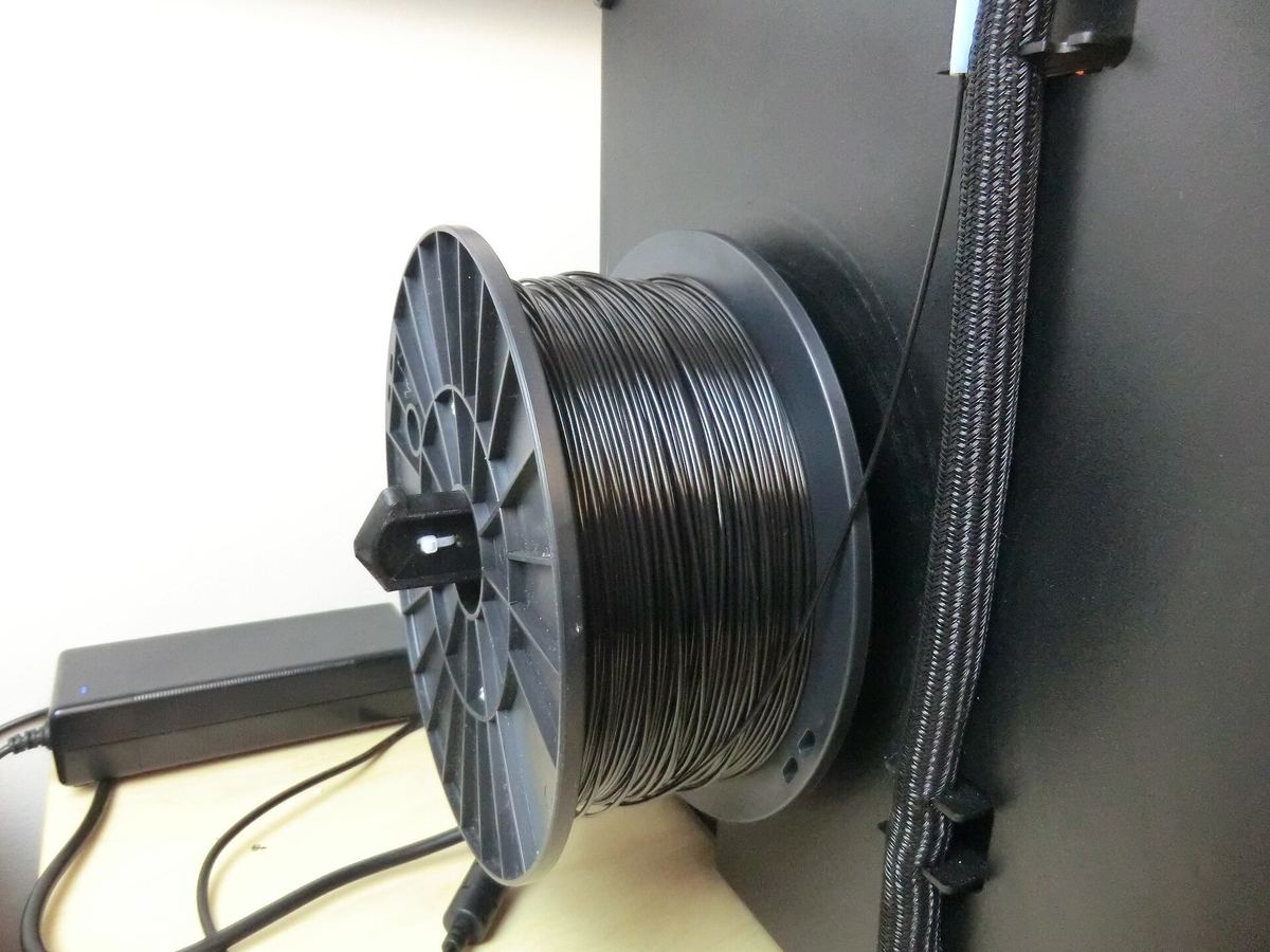 Rol zwart filament op een geprinte houder naast een printer