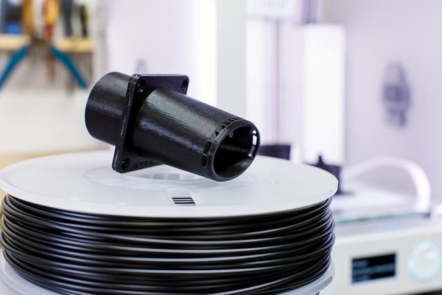 Zwart geprint technisch onderdeel met flens, op een rol filament